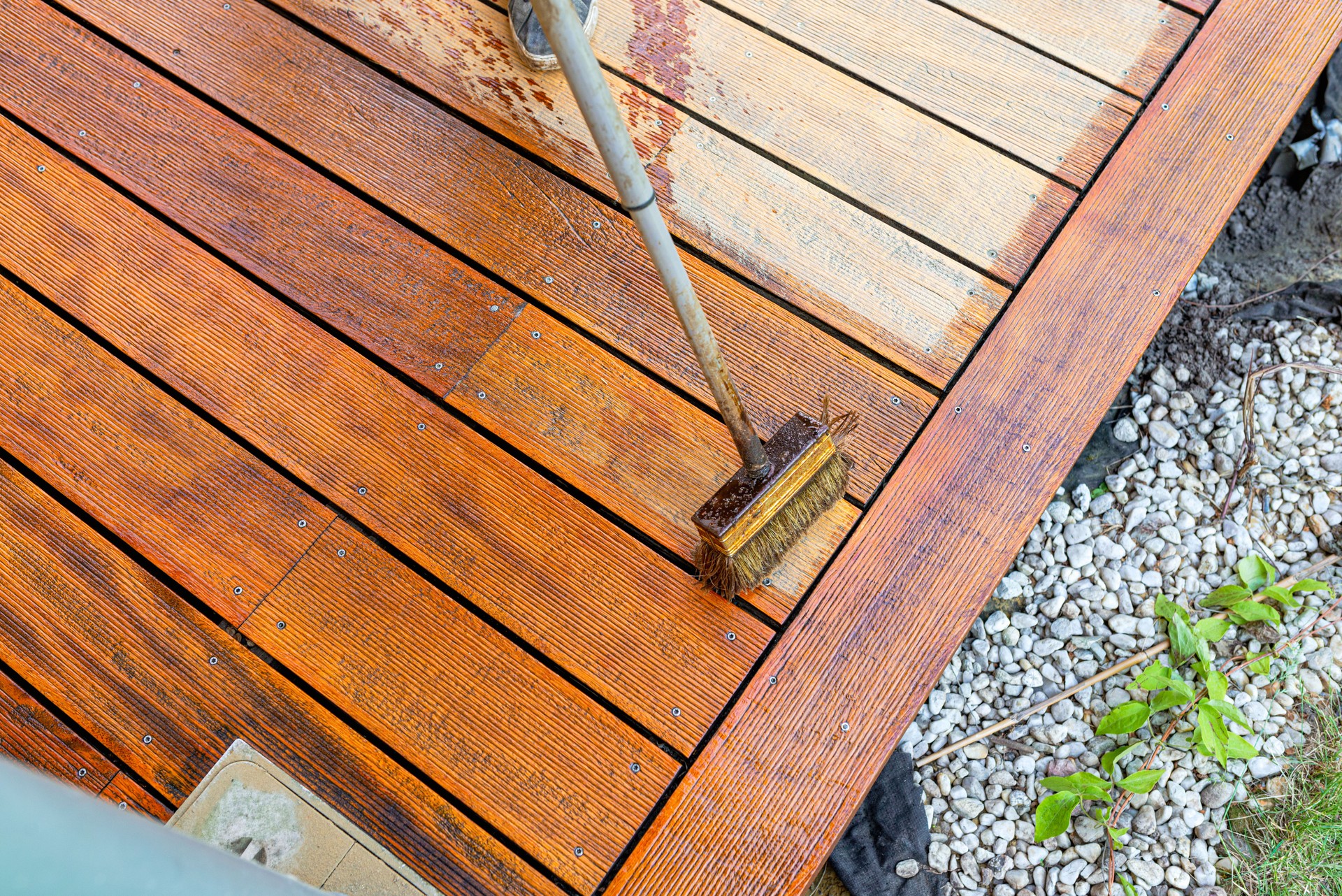Close-up of a wooden deck being stained with a brush for protection and maintenance during a home improvement project in bright sunlight